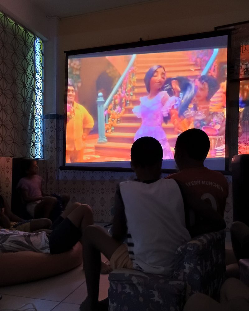 Crianças sentadas assistindo a um filme projetado na parede da Casa Amarela