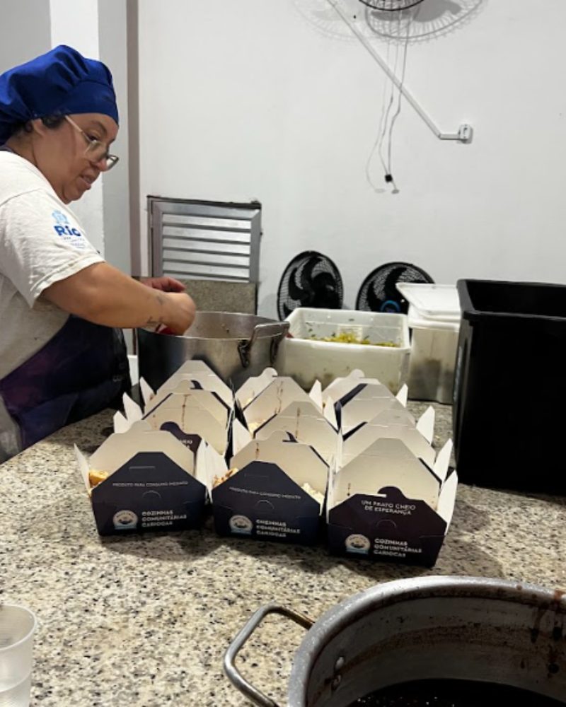 Cozinheira servindo marmitas na cozinha comunitária