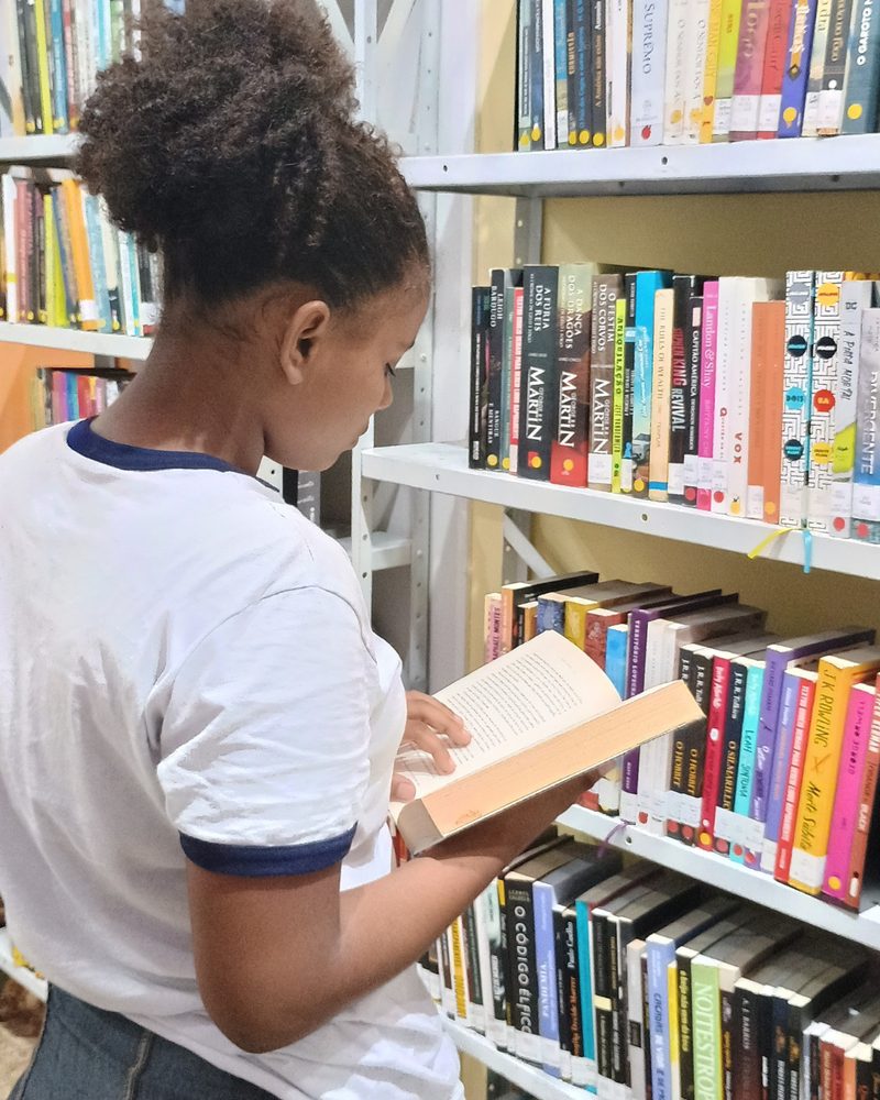 Menina de uniforme escolhendo um livro na estante da biblioteca