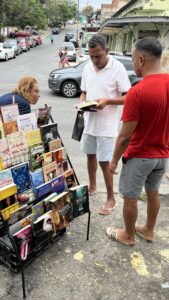 Carrinho de livros montado na calçada, com duas pessoas escolhendo títulos